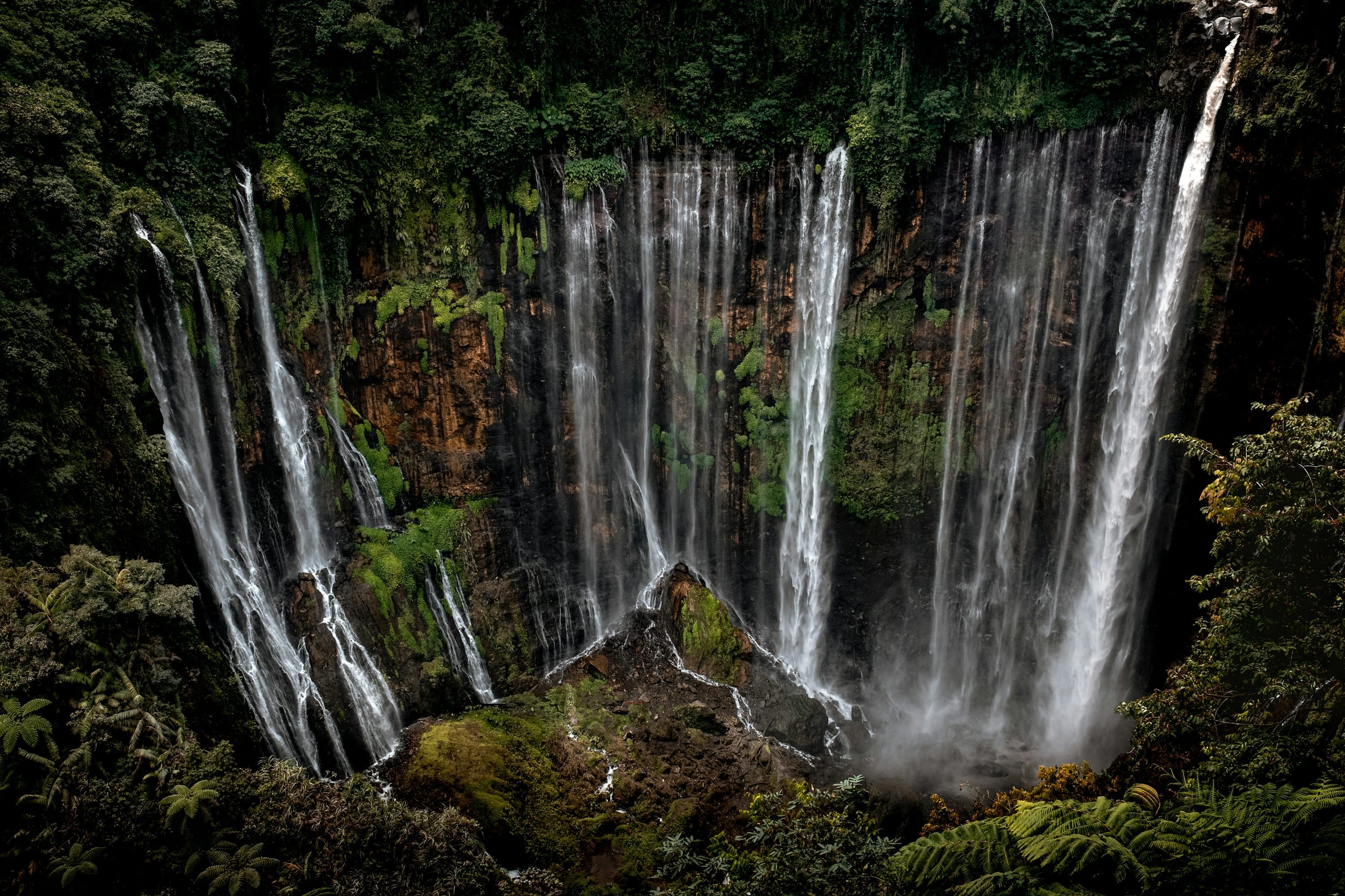 Air terjun Tumpak Sewu mengalir dari tebing hijau yang lebar seperti tirai