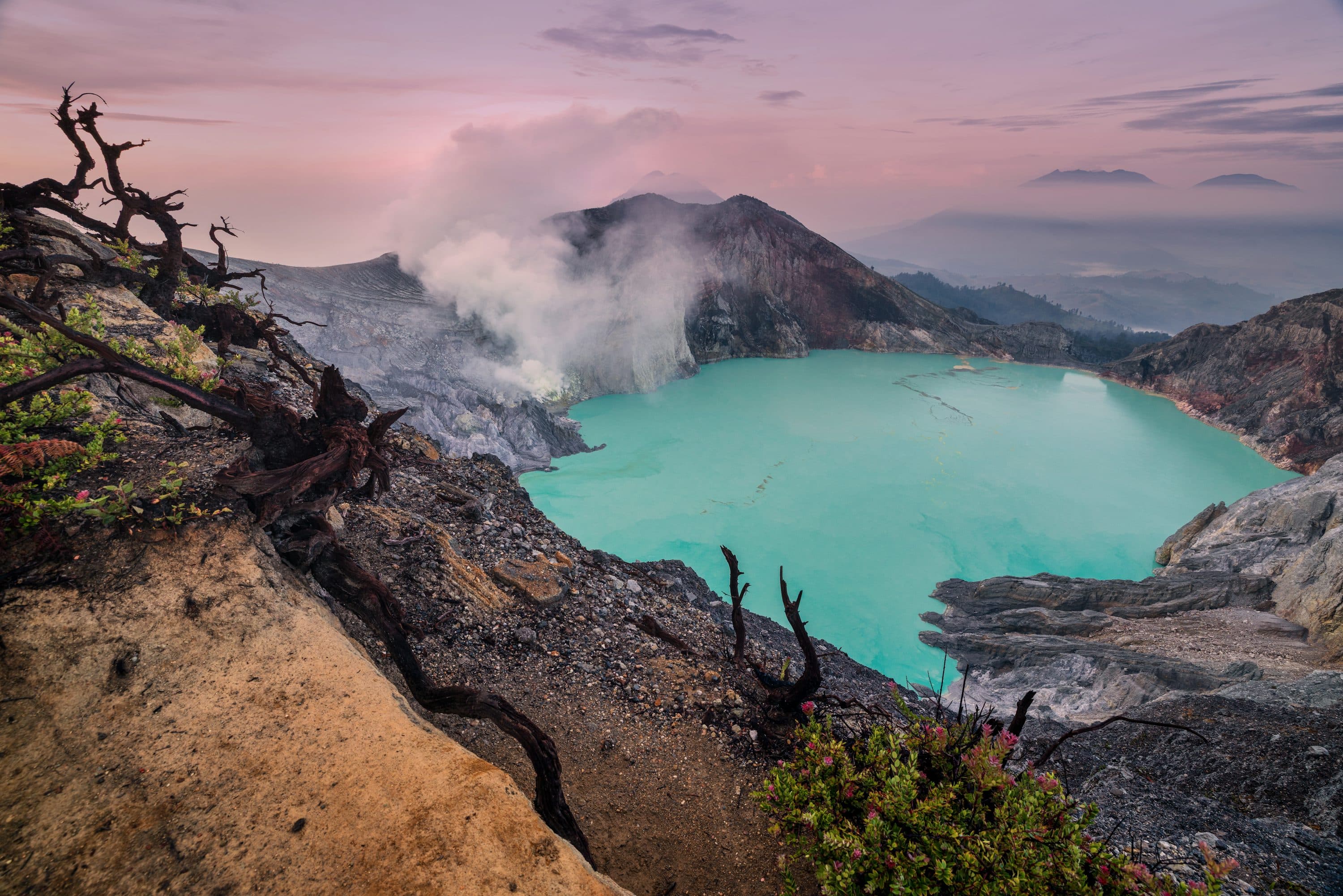 Danau kawah Ijen berwarna toska dikelilingi tebing batu dengan asap belerang